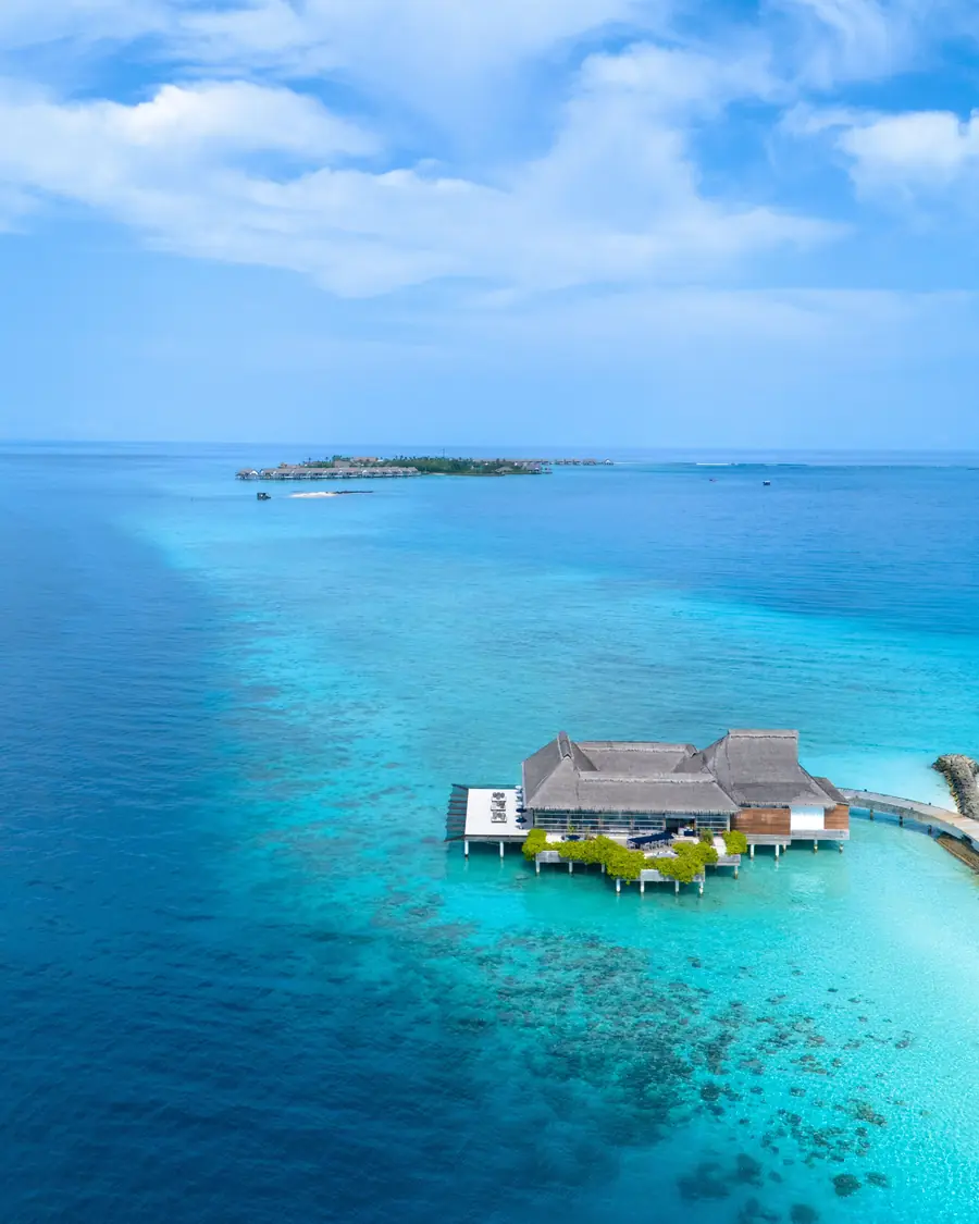 An overwater villa and its jetty alone in a turquoise lagoon in the Maldives, seen from the air