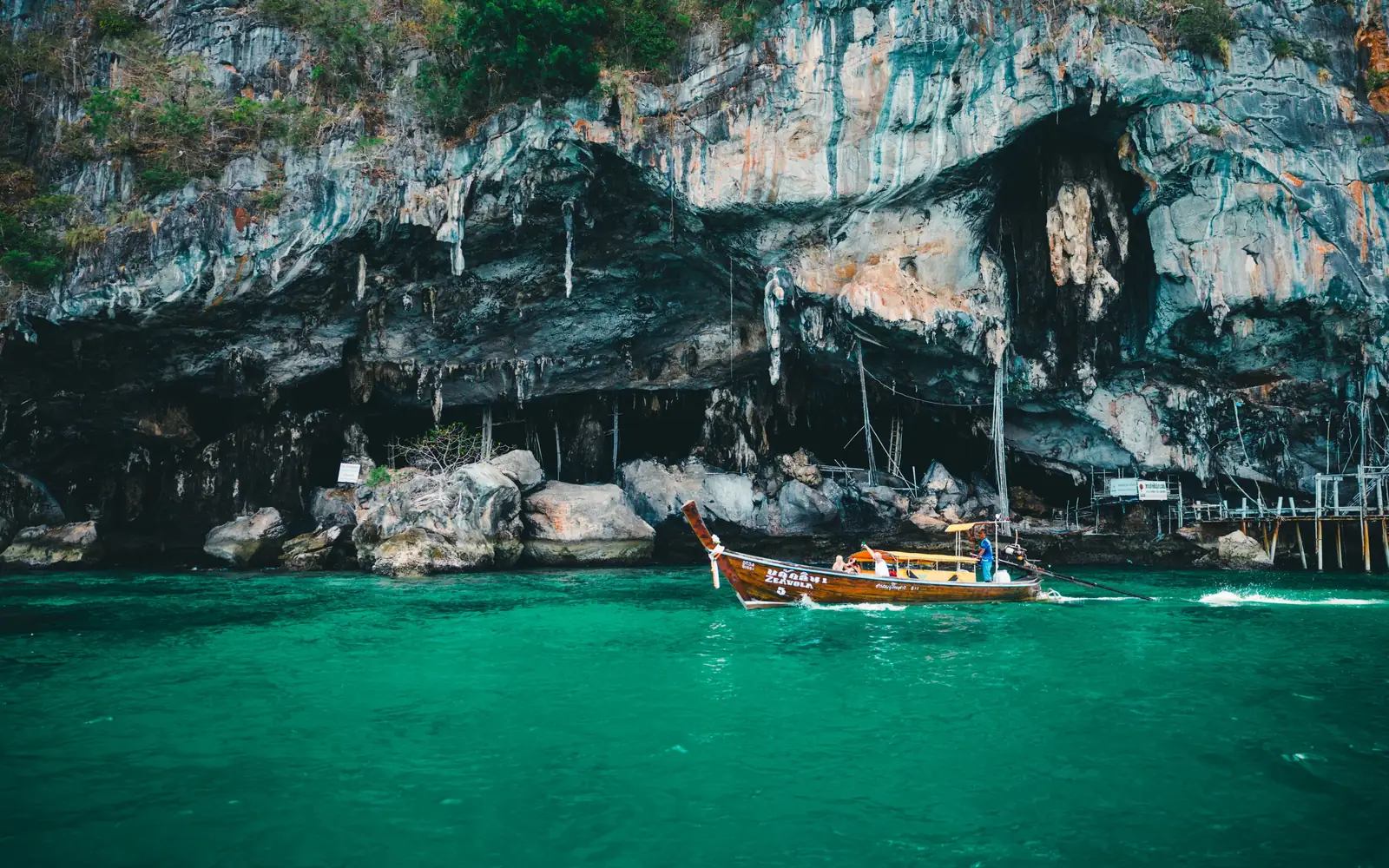 A longtail boat passing a limestone sea cave near Phuket, Thailand