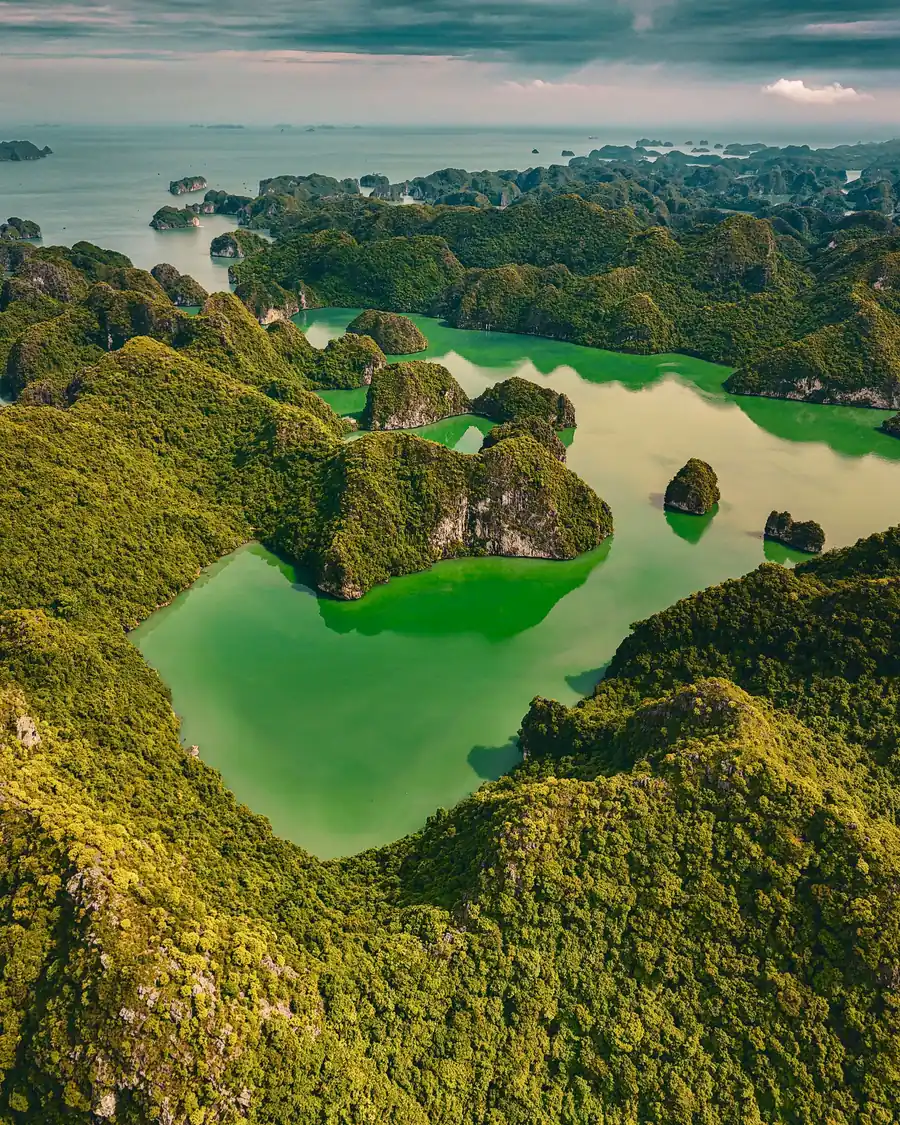 A green lagoon ringed by limestone hills in Ha Long Bay, Vietnam, seen from the air